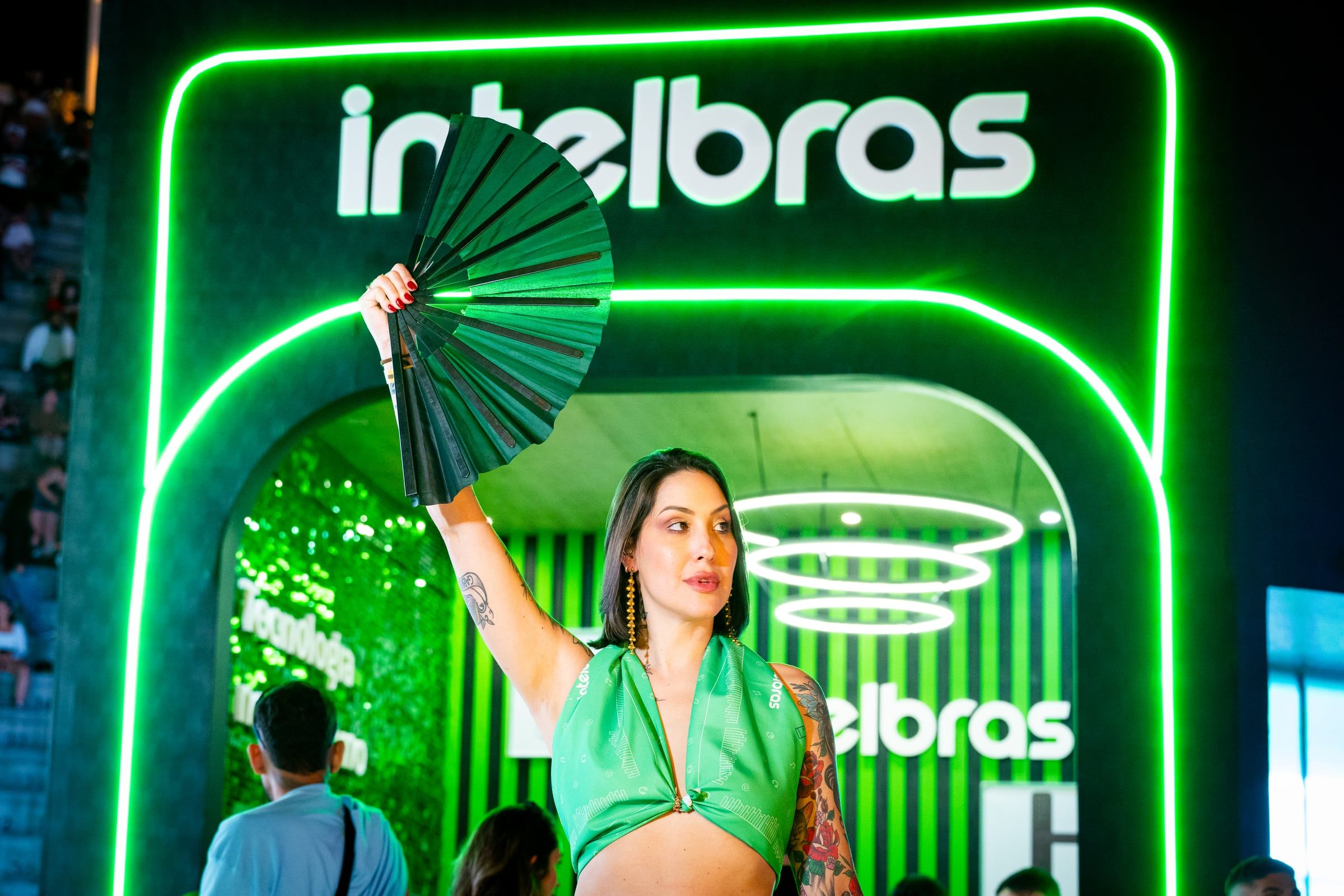 Mulher com leque verde diante do estande iluminado da Intelbras
