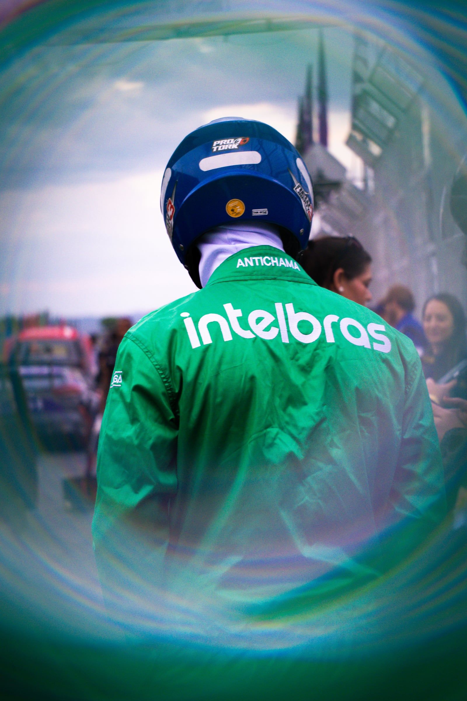 Piloto de capacete e jaqueta verde da Intelbras, visto de costas