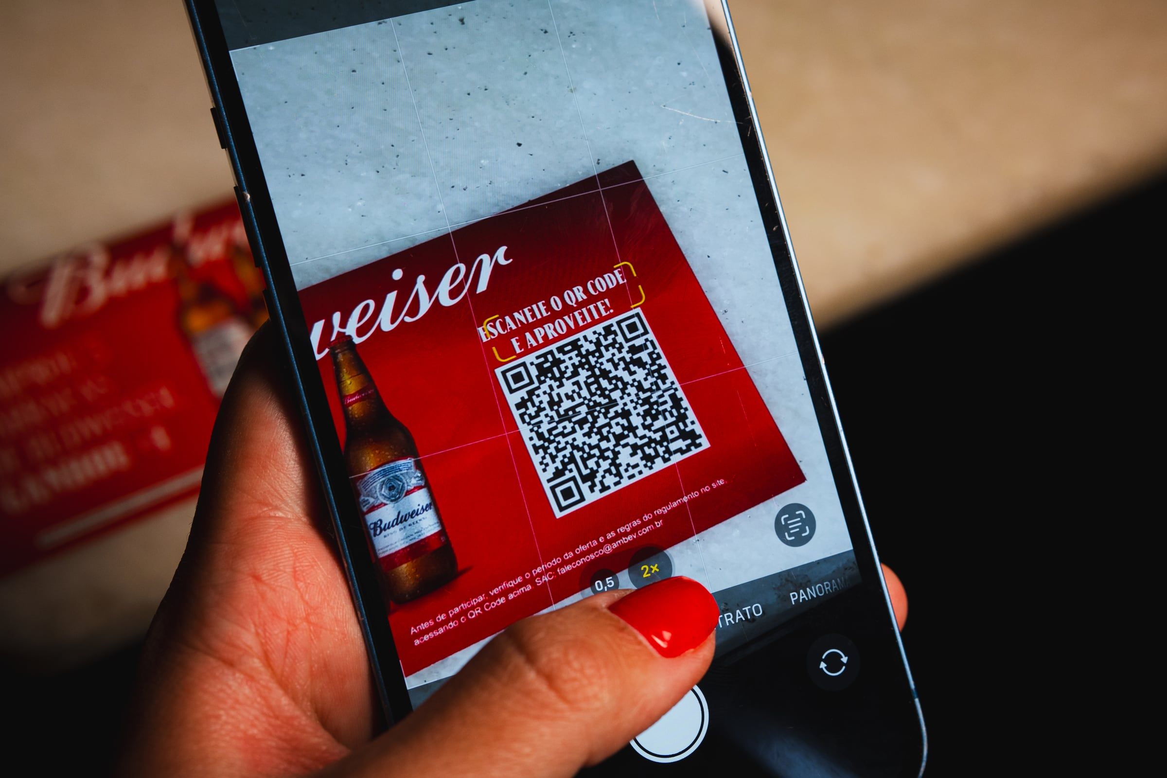 Mão segurando o celular para ler o QR code da promoção da Budweiser
