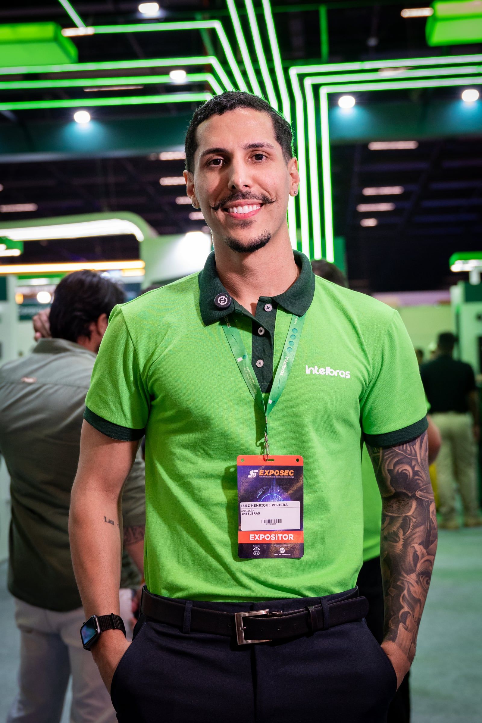 Promotor da Intelbras sorrindo, de crachá, no corredor da feira