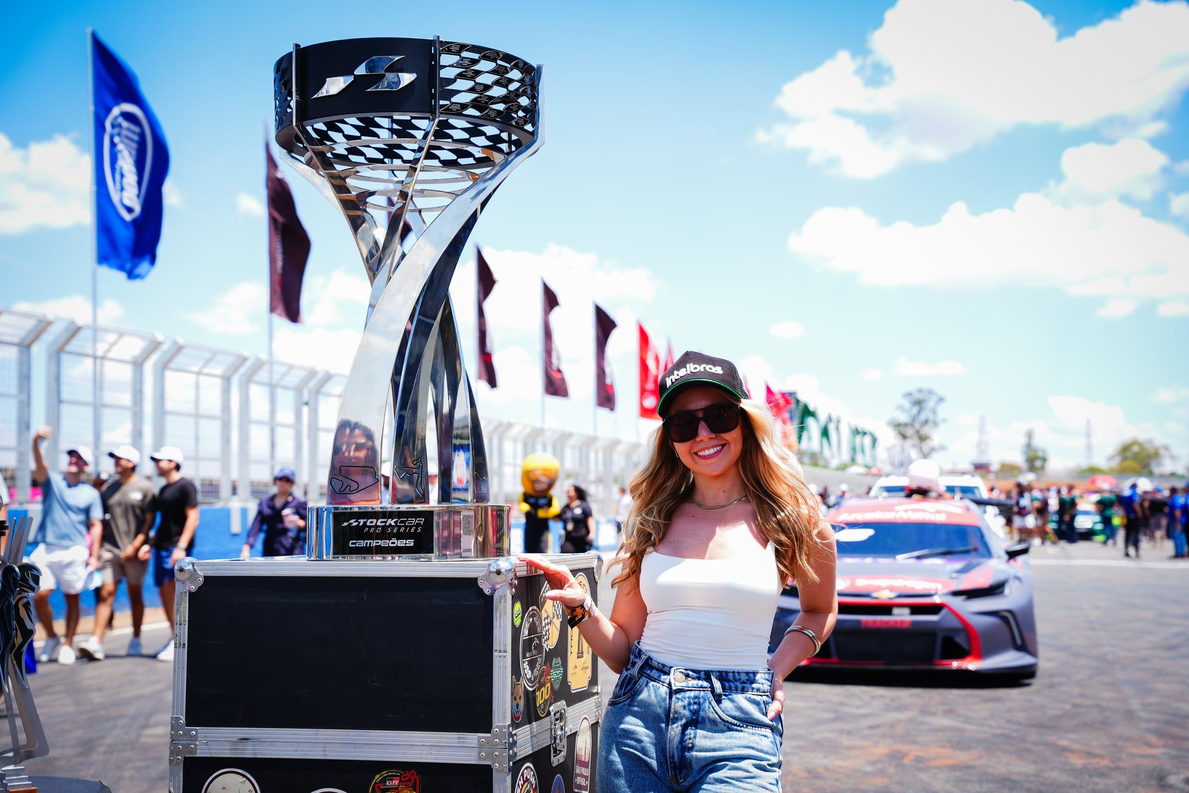 Mulher posando ao lado do troféu da Stock Car no grid