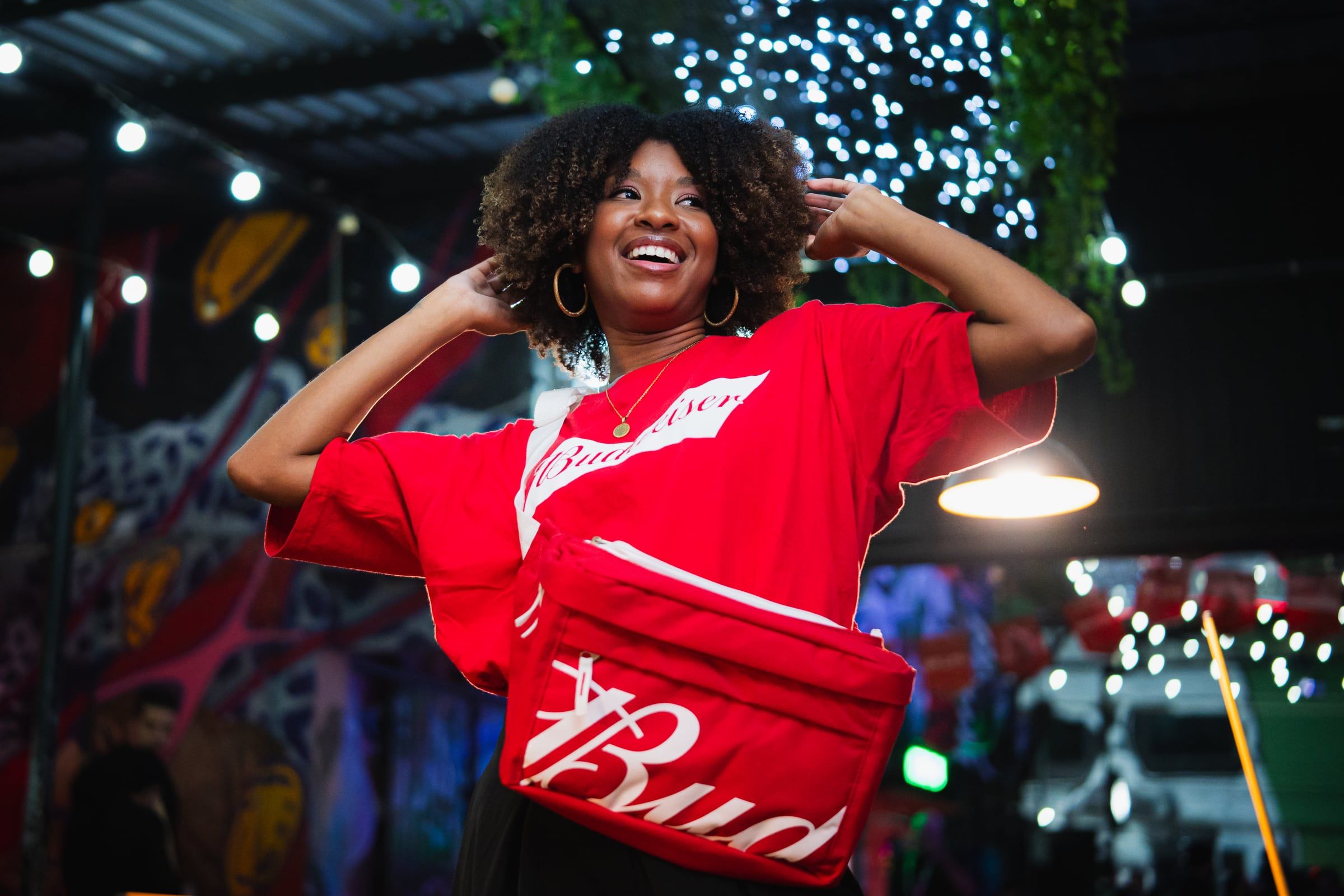 Mulher dançando com a bolsa vermelha da Bud, sob luzes de festa