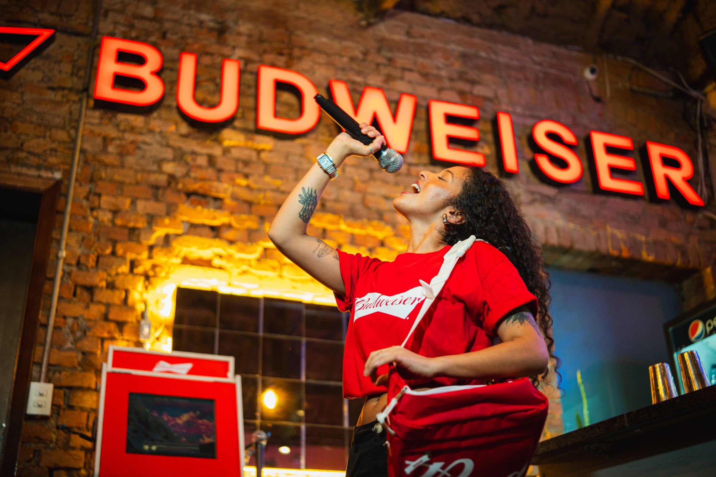 Mulher cantando no microfone diante do letreiro em neon da Budweiser